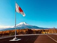 a japanese flag flies in front of a building with mt fuji in the background